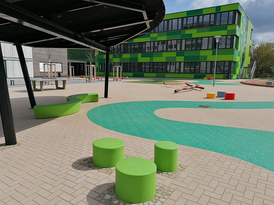 Ovales Dach, 3 grüne Hocker, grünes Band auf gepflastertem Hof, grüner Ergänzungsbau