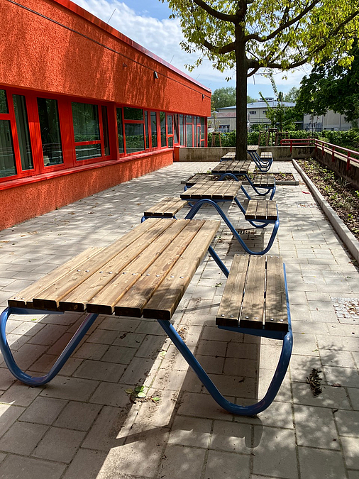 4 Tisch-Bank-Kombinationen auf Terrasse, dazwischen großer Baum