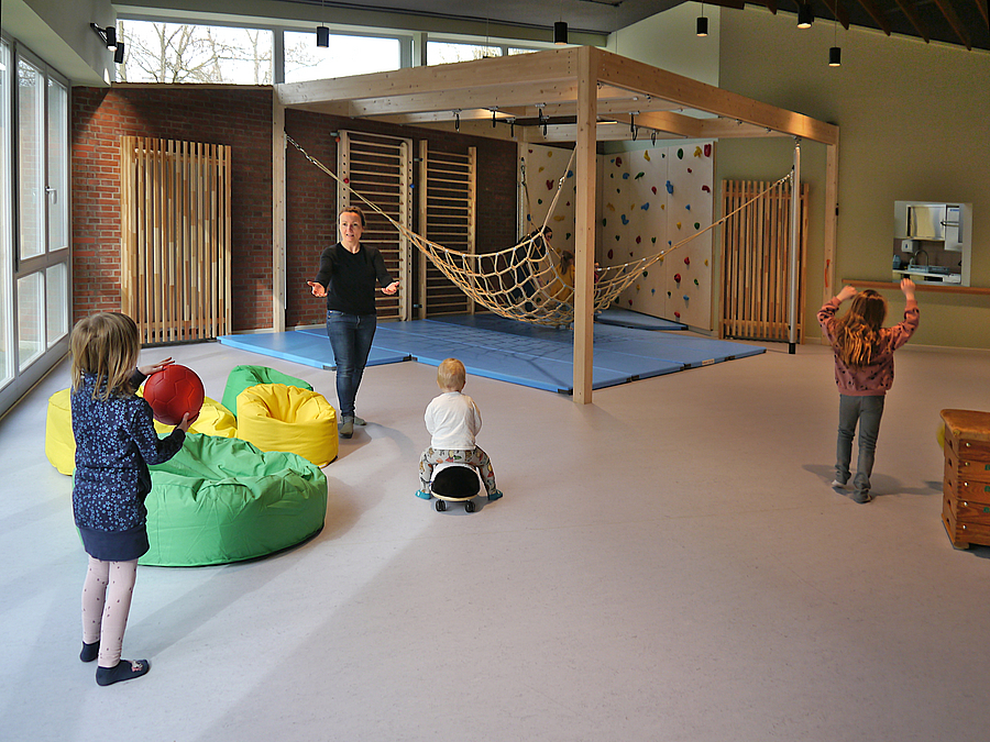 3 Kinder und Frau spielen in Raum mit Kletternetz und Boulderwand