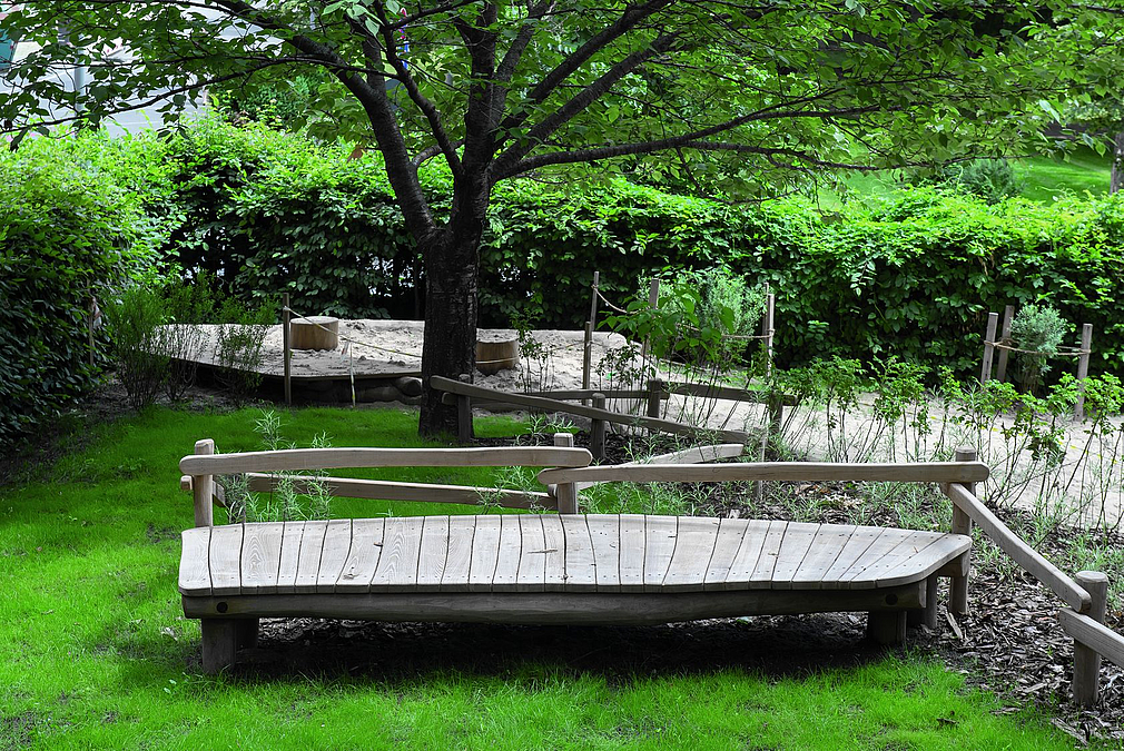 Holzdeck und gewundener Holzsteg auf Rasen unter Baum