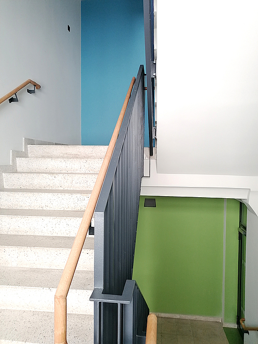 Wechsel vom grünen Erdgeschoss ins blaue 1. Obergeschoss mit dem Sozialpsychiatrischen Dienst und der Beratungsstelle für Menschen mit Behinderung und chronischen Krankheiten Treppenhaus mit Farbwechsel der Wandgestaltung zwischen zwei Geschossen