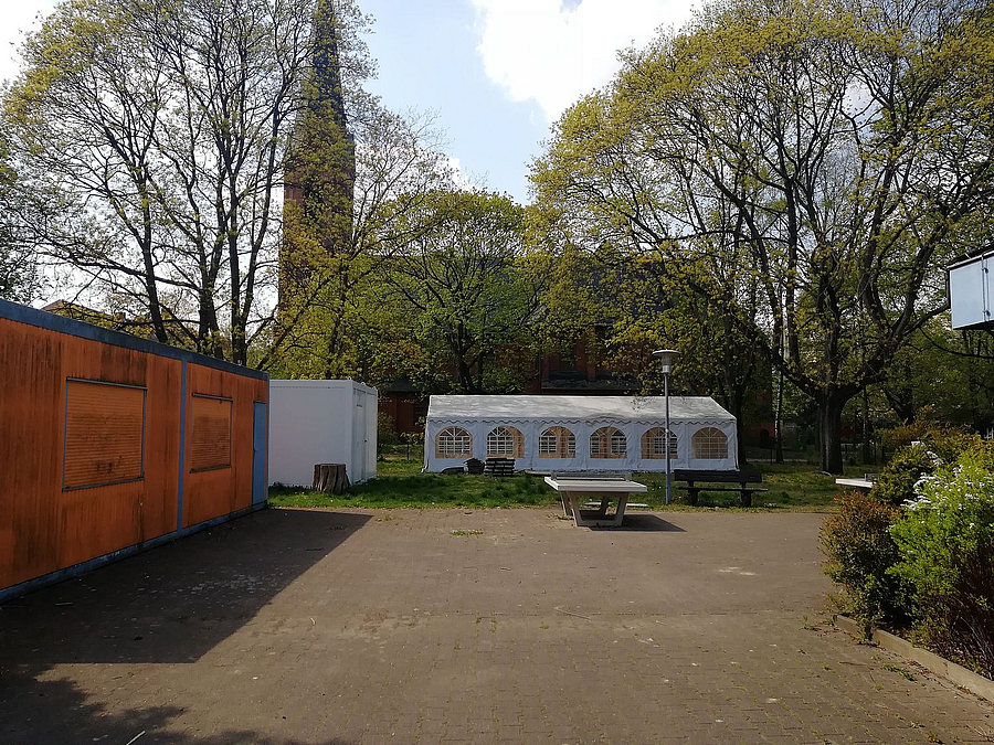 Pflasterfläche, Partyzelt, rötlicher Container, dahinter Kirche