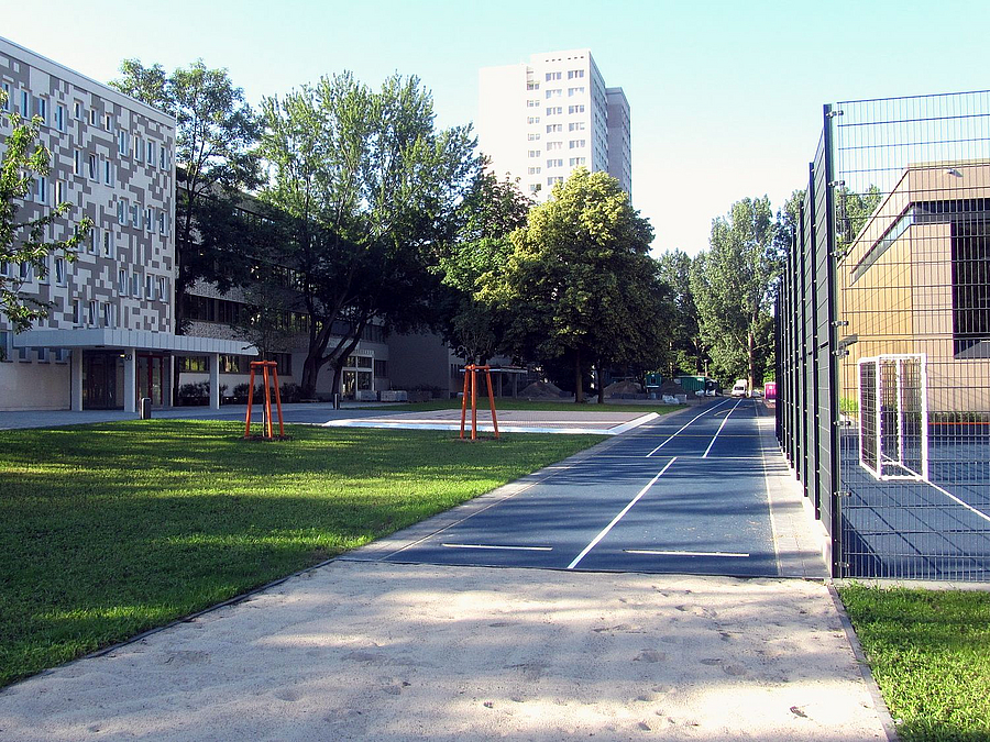 Schulhaus, Grünfläche, Laufbahn, Ballfangzaun