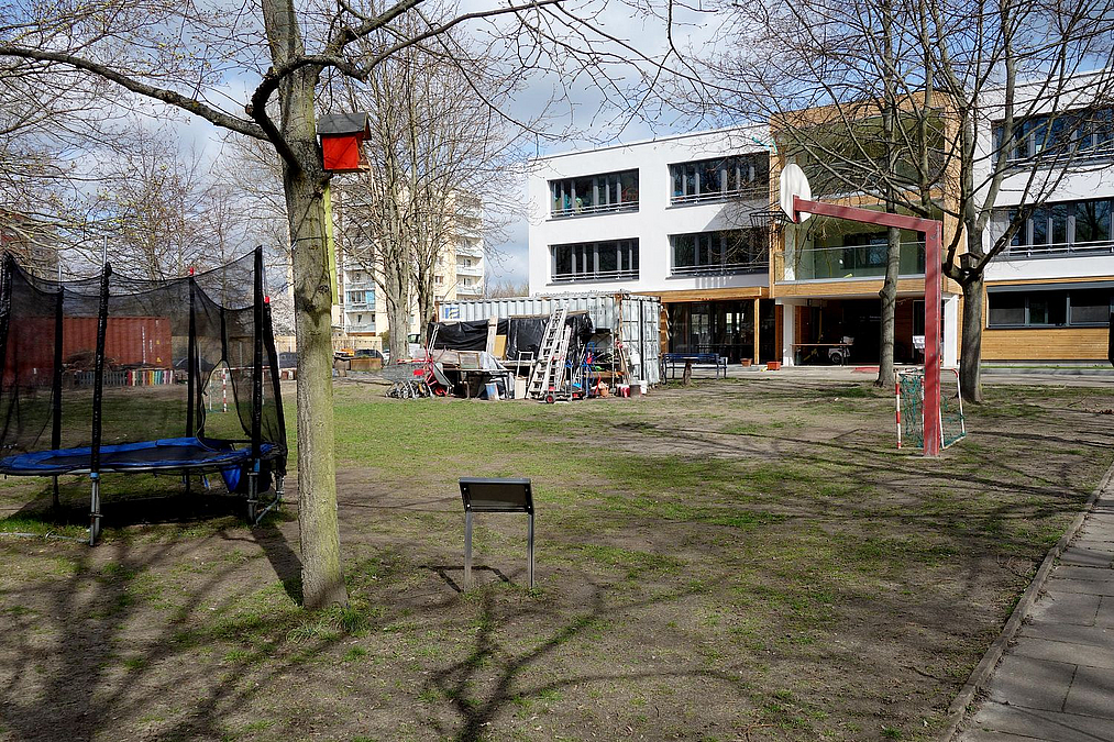 Helles dreistöckiges Gebäude, Rasenfläche, Trampolin, Container mit Geräten