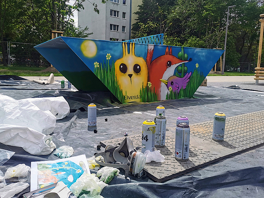 Tierisches Dorfleben gestalteten Kinder und Jugendliche für die Tischtennisplatte am Spielplatz Trapezförmig aufgebaute Tischtennissplatte mit gestalteter Seitenwand: Comic-Zeichnung Fuchs und Hase, davor Sprühflaschen