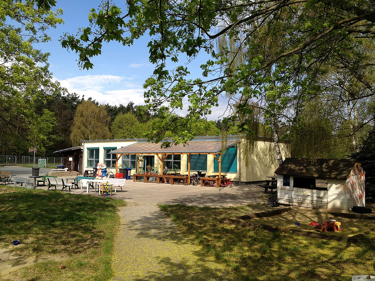 Flachbau mit Vordach, Terrasse mit Holztischen und Bänken, Spielgarten