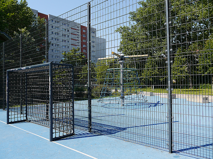 Blick durch Ballfangzaun auf Kletterdrehnetz, alles auf blauem Boden