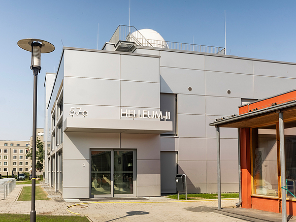 Graue Fassade Helleum II mit Observatorium und Schriftzug über dem Eingang, im Anschnitt das orangefarbene HELLEUM I