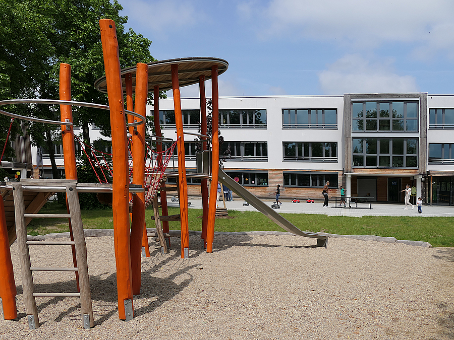 Rutschenturm in orangefarbenem Holz, Rasen, sanierter Kita-Typenbau in Weiß und Holz