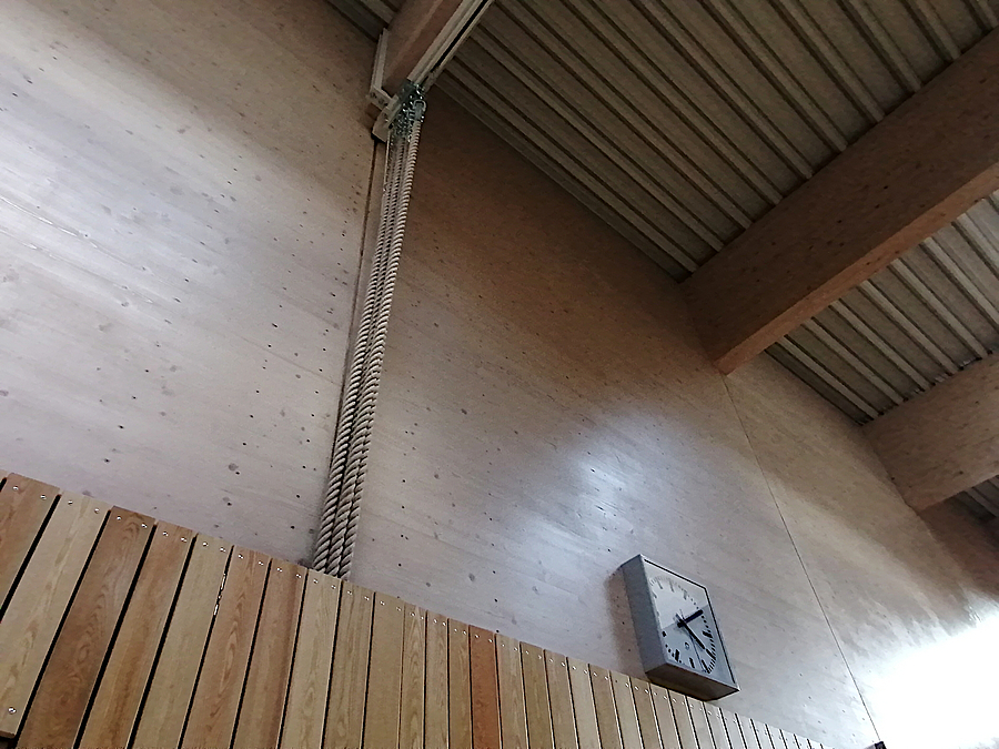 Prallwand und Holzwand mit Uhr, hölzerne Balken, Profildecke schräg von unten