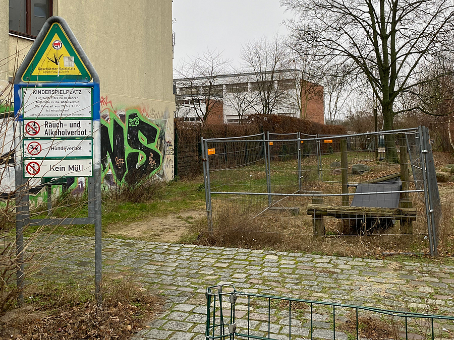 Spielplatzschild und gesperrtes Spielgerät neben Hauswand