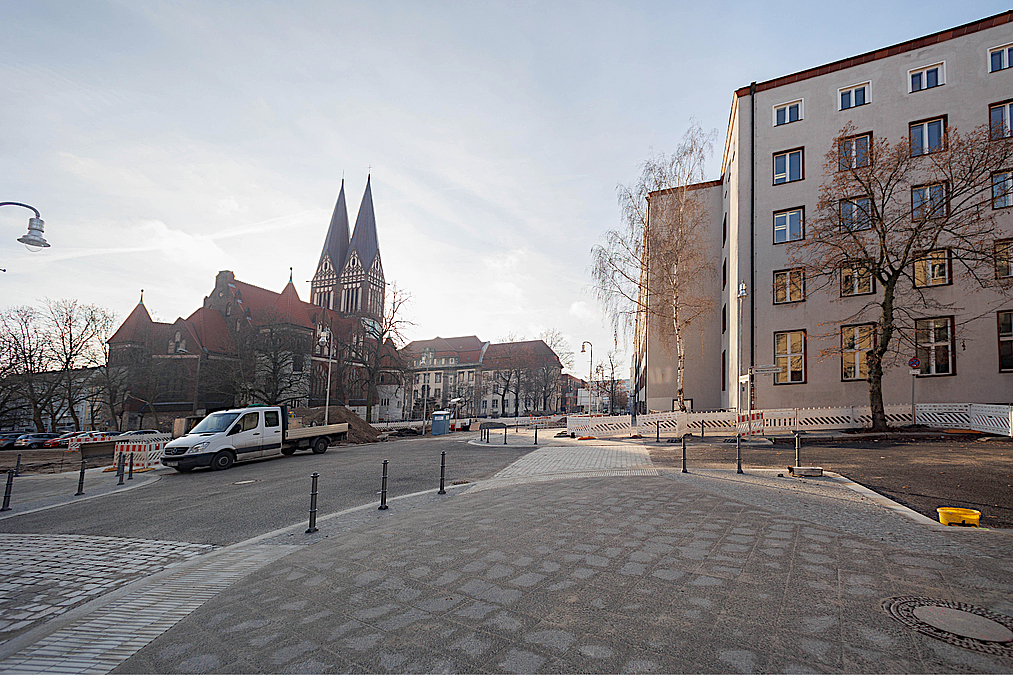 Kirche, Straßenraum mit Pollern und gepflasterter Querung