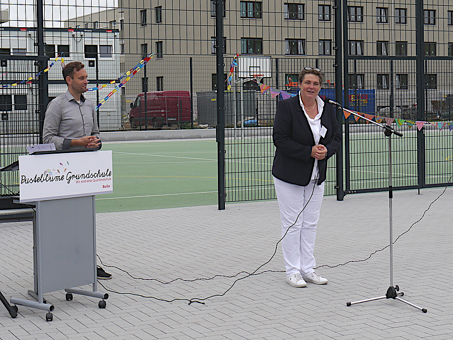 Rednerin und Moderator vor Ballspielplatz