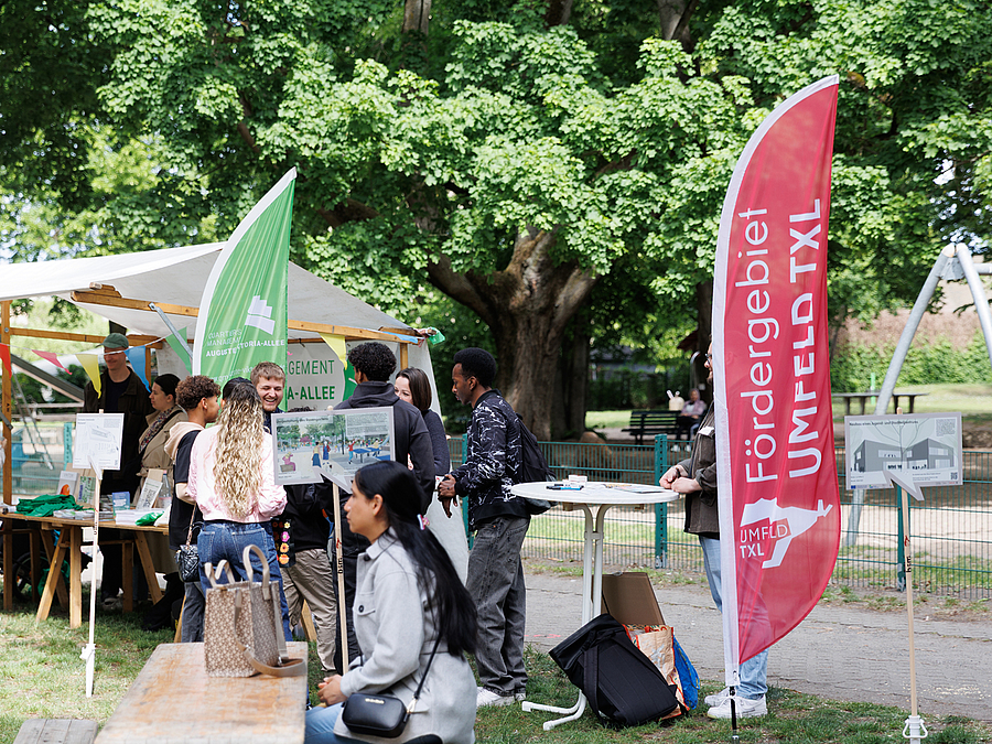 Fest rund um die Segenskirche im Auguste-Viktoria-Kiez am Tag der Städtebauförderung 2025 Fest mit Menschen und Fahnen mit Aufschrift "Fördergebiet Umfeld TXL"