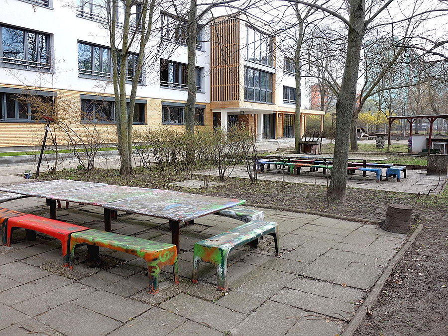 Helles dreistöckiges Gebäude, davor Tisch-bank-Gruppe für Kleinkinder, winterliche Bäume