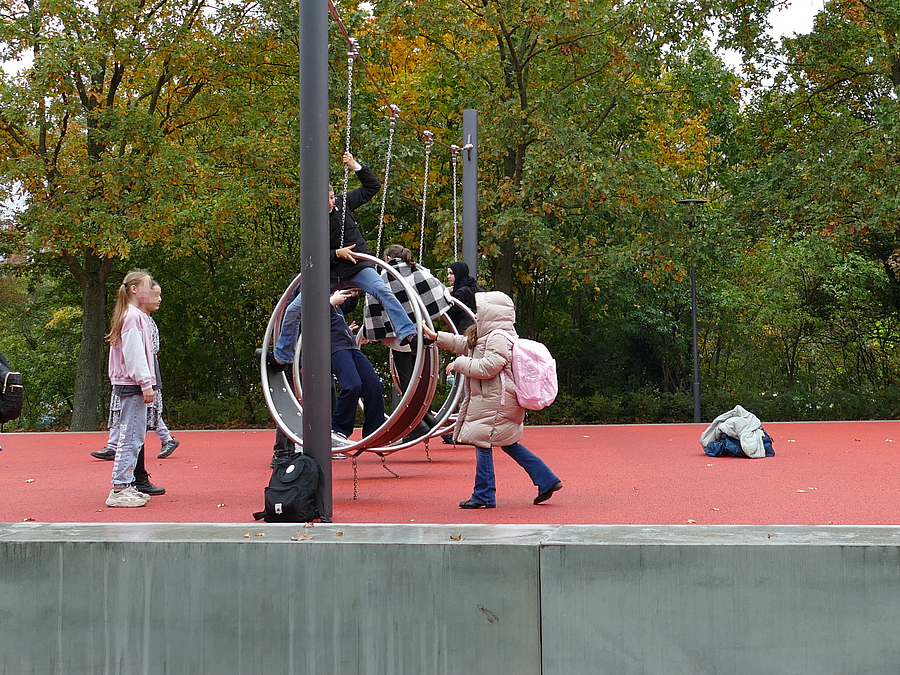 Kinder spielen an großen Reifenschaukeln aus Stahl und Gummi auf rotem Belag