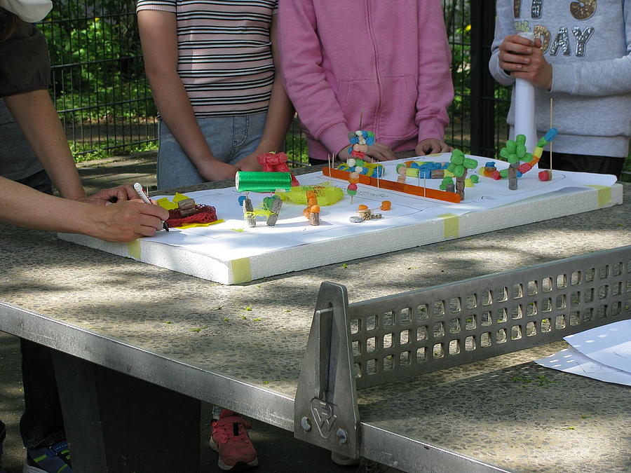 Hände am Spielplatzmodell aus Playmais auf Tischtennisplatte