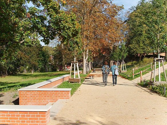 2 Menschen auf Weg im Park, Klinkermauer stützt Geländestufe