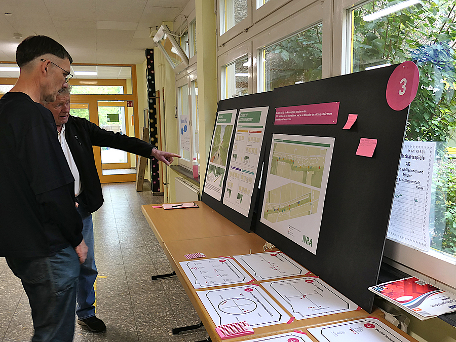 Zwei Männer im Gespräch vor Stand mit Blättern und Plänen