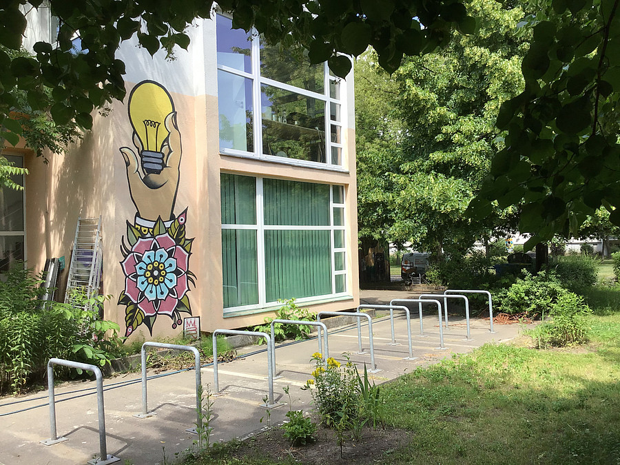 Zweistöckiges Gebäude mit bodentiefen Fenstern, Wandbild und Fahrradbügeln