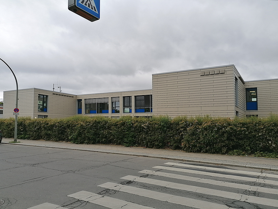 zweistöckiger, heller Flachbau mit zurückgesetztem Mittelteil an einer Straße