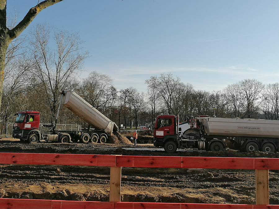 2 Baufahrzeuge, eins schüttet Erde in Grube
