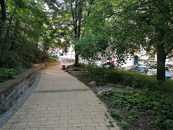 Gepflasterter abwärts führender Weg, Querrinne, Kiesbett unter Bäumen