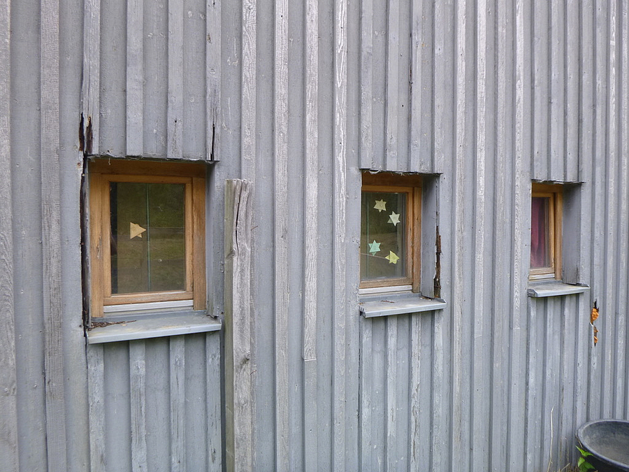 Schäden an der Holzfassade mit drei kleinen Fenstern
