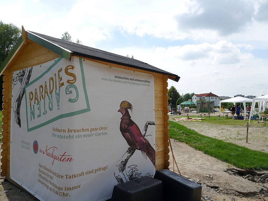 Schuppen mit um die Ecke geklebtem, wandfüllenden Plakat "Paradiesgärten" mit Zeichnung Paradiesvogel
