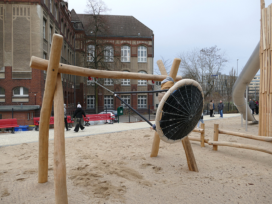 Spielplatz mit Tunnelrutsche und Nestschaukel in Bewegung, im Hintergrund Teske-Schule