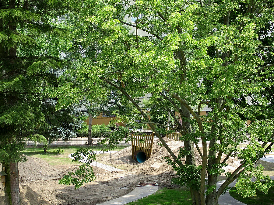 Blick auf die Baustelle Blick durch Bäume auf Sandhügel mit Tunneleingang