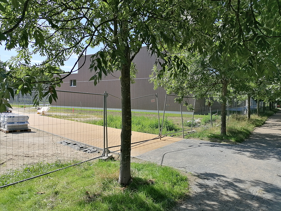 Zukünftiger Eingang zum Parkweg über die Werneuchener Wiese Neuer Weg hinter Bauzaun und Bäumen