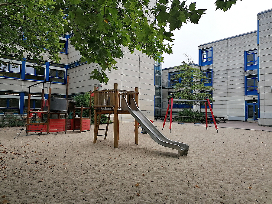 Die große Sandspielfläche ist das Herz des Grundschulhofes Helle Sehulgebäude, Sandfläche mit Rutsche und mehr, Laubbaum