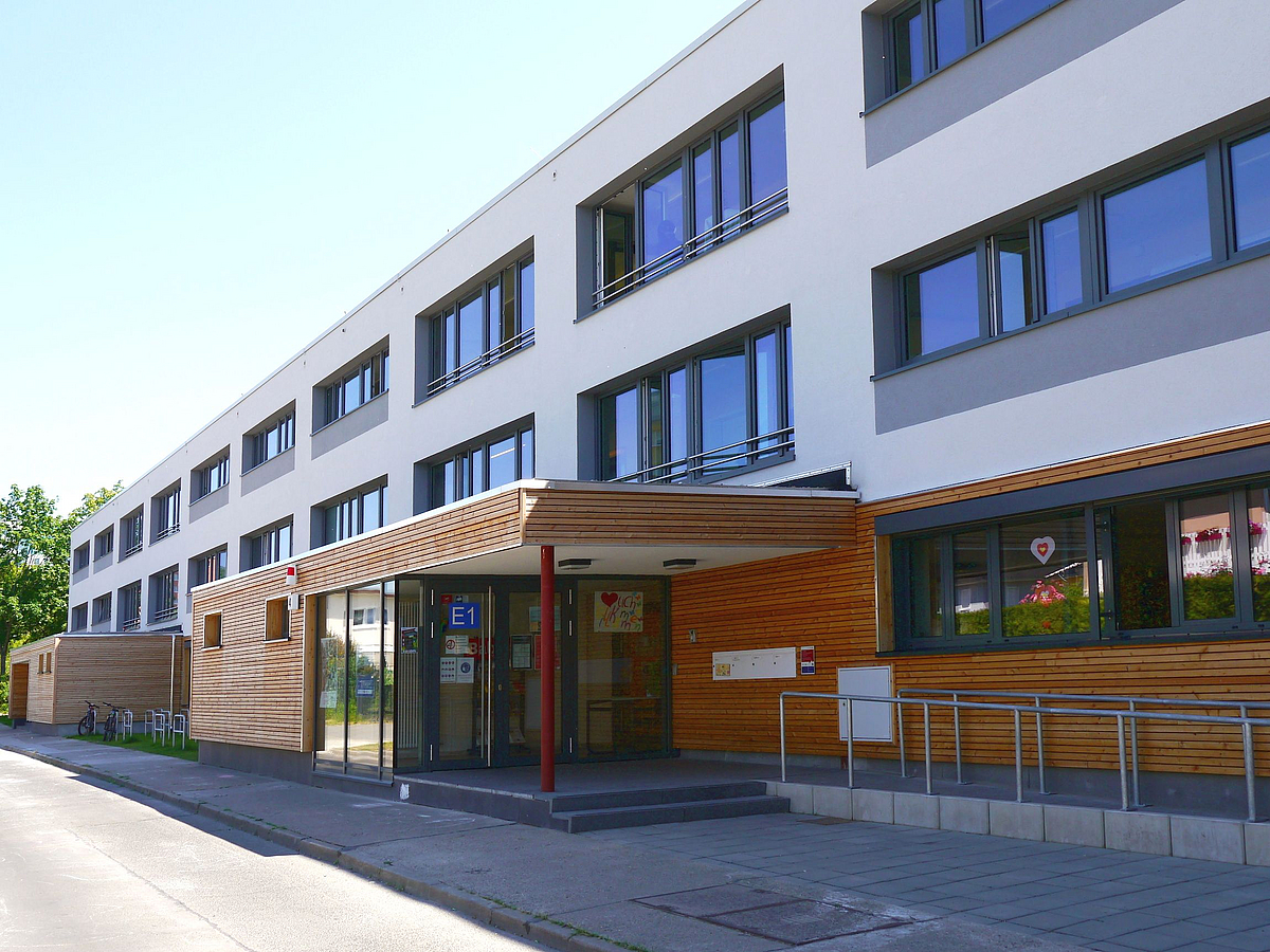 Lang, helle Fassade mit holzverkleidetem Erdgeschoss