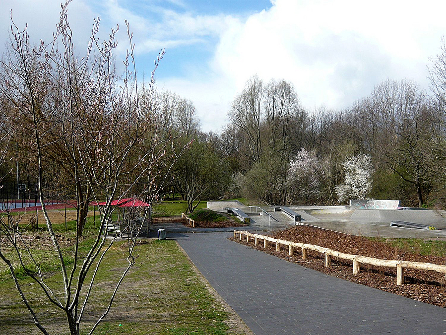 Gepflasterter Weg, Rasen und junger Baum im Frühling, im Hintergrund roter Pavillon