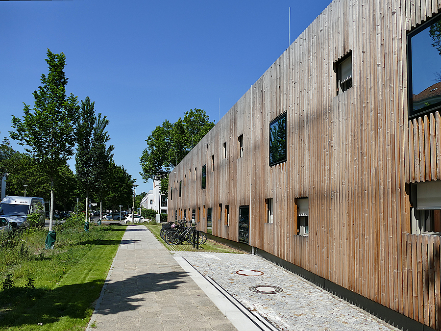 Holzlatten-Fassade eines zweistöckigen Gebäudes mit asymmetrischen Fenstern, Weg