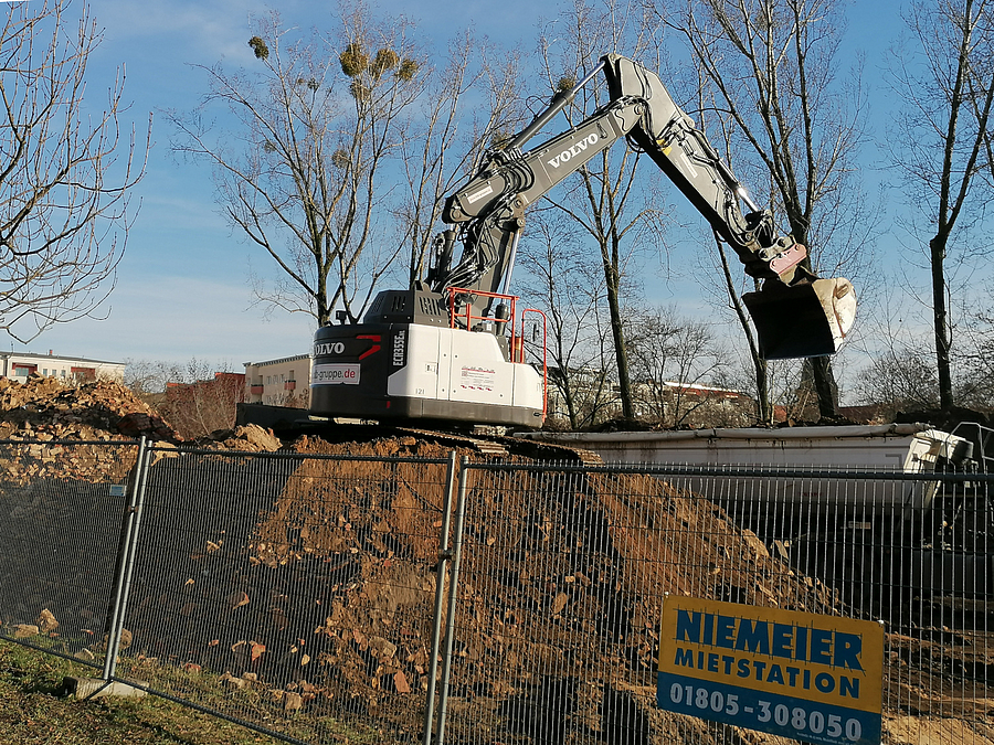 Raupenbagger arbeitet auf großem Haufwerk mit Erde und Trümmern