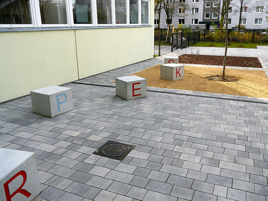Pflasterfläche, Betonwürfel mit Buchstaben, neu gepflanzter Baum