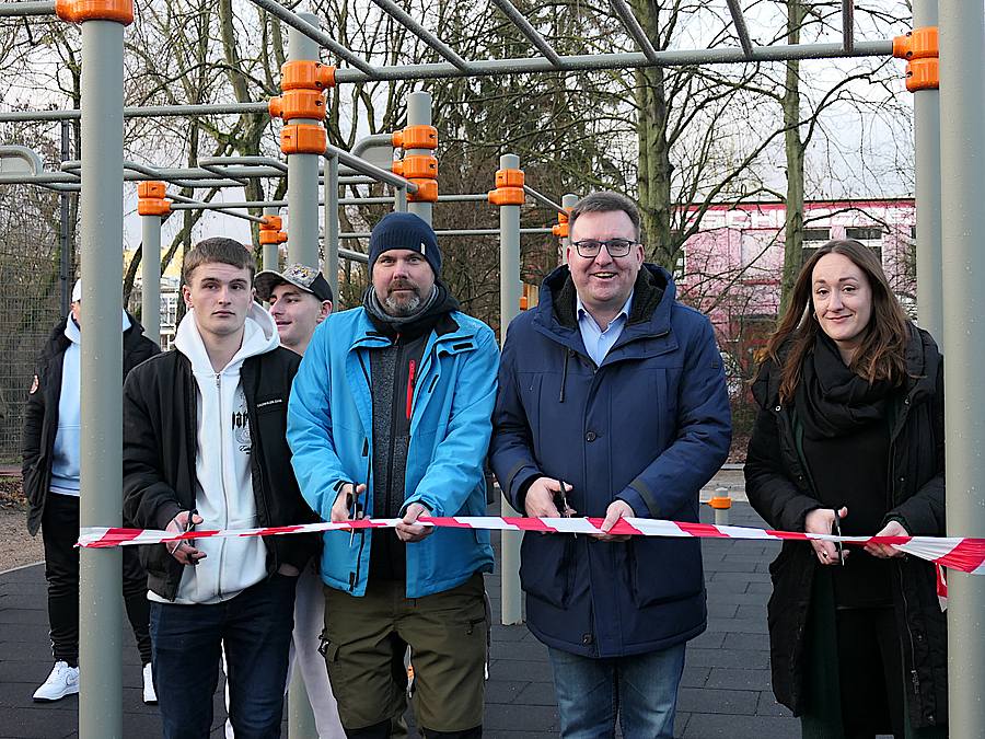 Natali Hellenkamp vom SGA, Bezirksstadtrat Thorsten Schatz, der Leiter des Geschwister-Scholl-Hauses, Daniel Borrmann und ein Jugendlicher (von rechts) bei der Eröffnung am 20.12.2023 4 Männer und eine Frau mit Schere am Flatterband vor der Calisthenics-Anlage