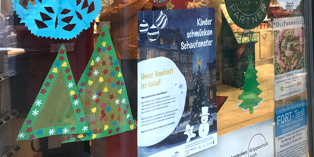 Gebastelte Weihnachtsdeko im Fenster und Plakat: Kinder schmücken Schaufenster