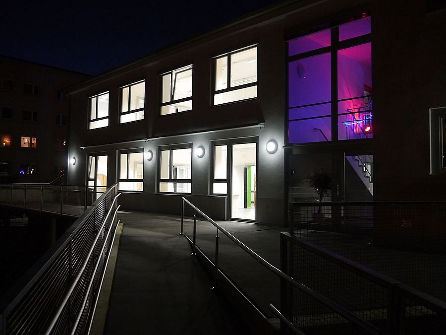 Die Gartenfront der Kita mit der Rampe in der Dezembernacht Gebäue mit Rampe im Dunkeln, ein Fenster violett beleuchtet