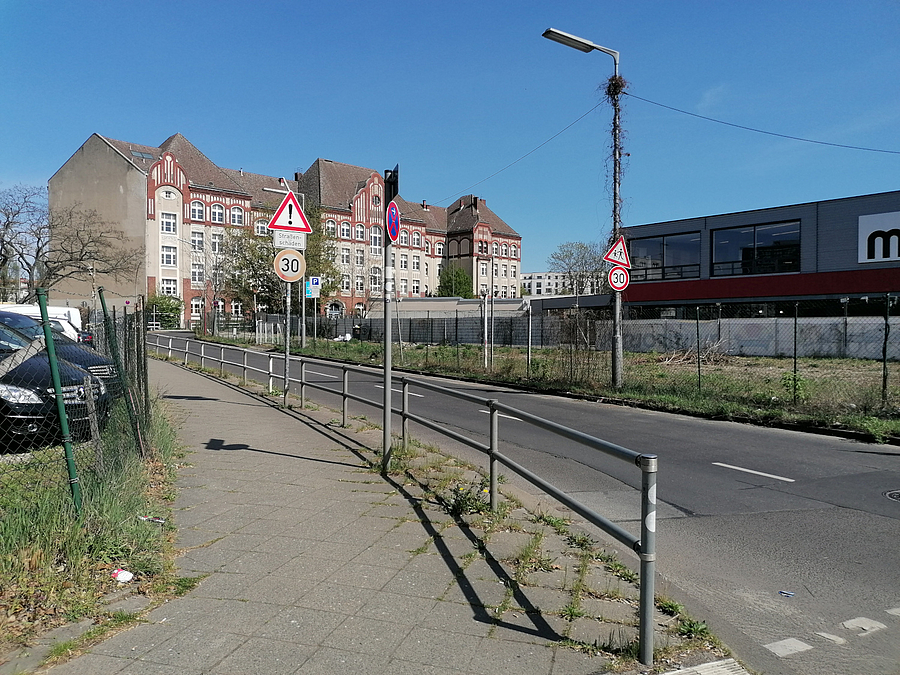 Schmale Straße mit einseitigem Fußweg und Geländer, Blick auf altes Schulgebäude