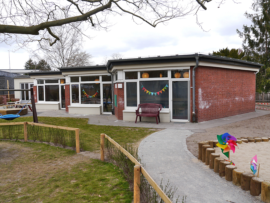 Sechseckige Bauteile, aneiandergereiht, Ziegel und weiß verputzt, davor Spielplatz