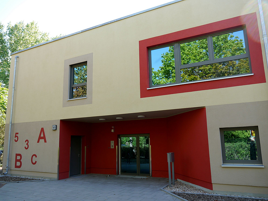 2-Geschosser in Beige mit rot abgesetztem zurückliegenden Eingang und Buchstaben-Zahlen-Muster