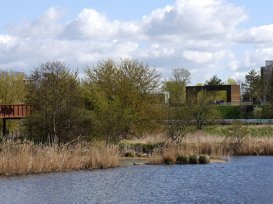 Blick über Teich auf Cortenstahlsteg und -rahmen 