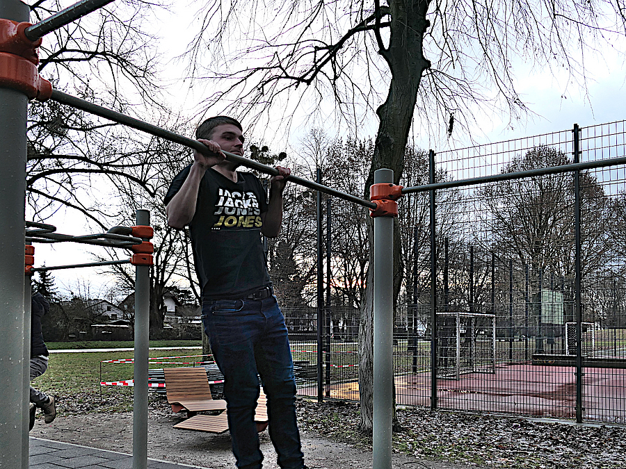 Klimmzug zur Probe. Bis richtig trainiert werden kann, muss noch bis zum Frühjahr gewartet werden Junger Mann macht Klimmzug an Reckstange der Anlage