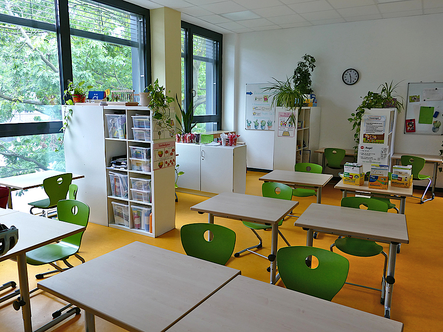 Unterrichtsraum mit großen Fenstern, gelbem Boden und hellen Möbeln