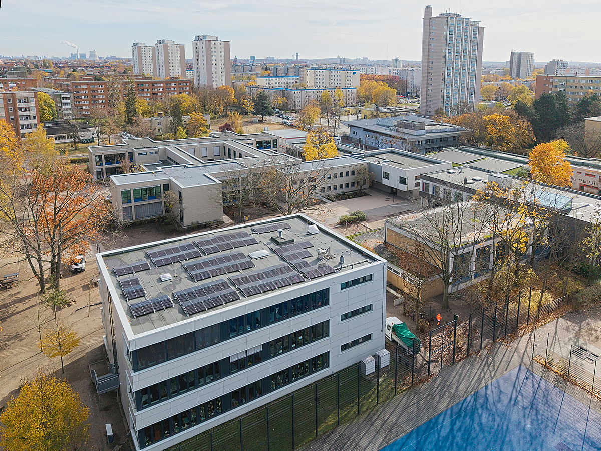 Schrägluftbild im Herbst mit modernem Schulergänzungsbau (MEB) vorn und Hochhäusern im Hintergrund