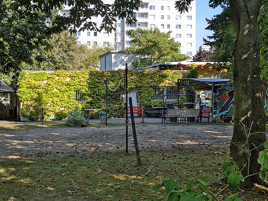 Garten mit Beachballfläche und Hollywood-Schaukel, niedriger Seitenflügel mit vergitterten Fenstern mit wildem Wein, dahinter Hochhaus