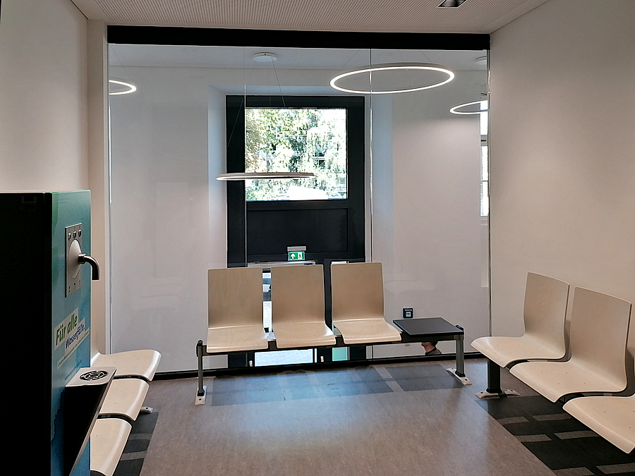 Neuer, freundlicher Wartebereich über dem Eingang Wartebereich mit Wasserspender und kreisförigen Deckenlampen